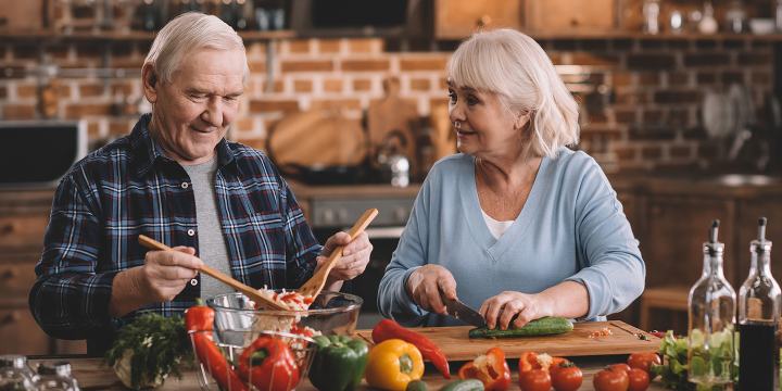 portrait of smiling senior couple making salad together in kitchen